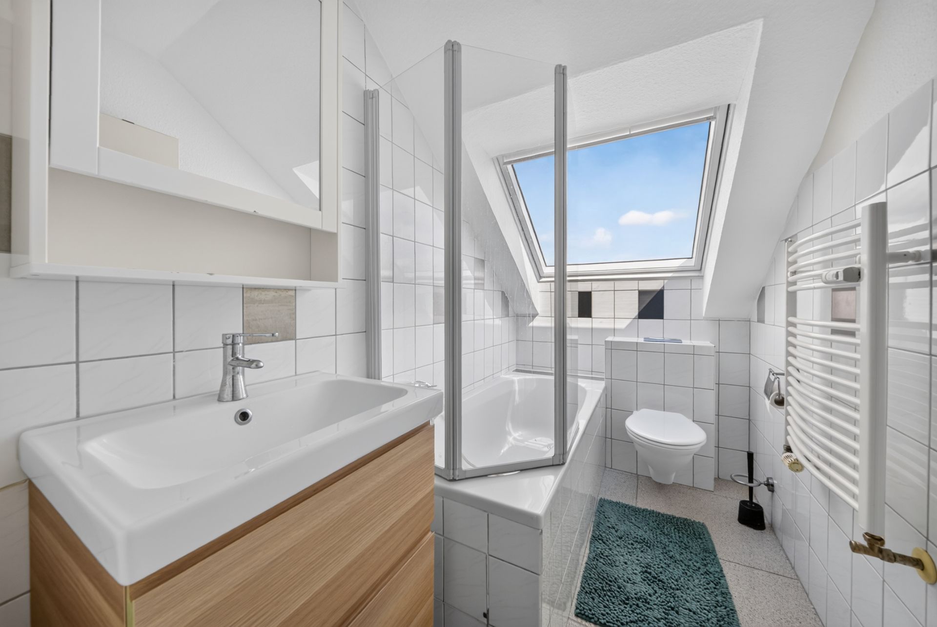 Modernes Bad mit Dachfenster, Waschbecken, Badewanne, WC und Heizkörper.