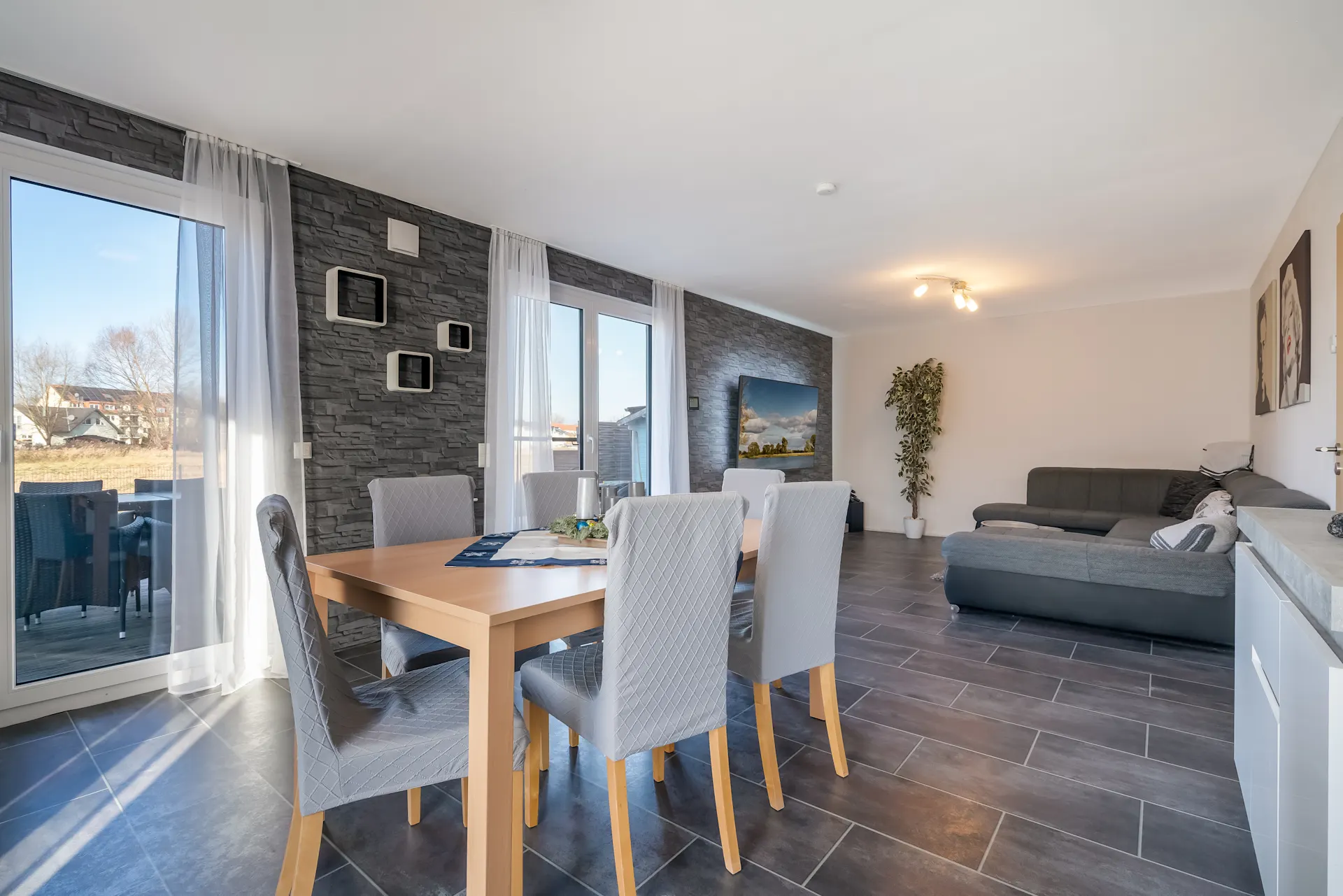 Modernes Wohnzimmer mit Essbereich, großem Tisch, grauer Couch und Steinwand.