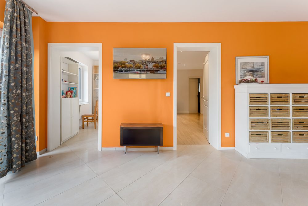 Wohnzimmer mit orangefarbener Wand, zwei offenen Türen, Kommode mit Körben und Vorhängen links.