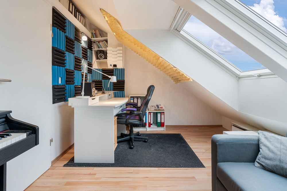 Arbeitszimmer im Dachgeschoss mit Schreibtisch, Drehstuhl und großem Dachfenster.