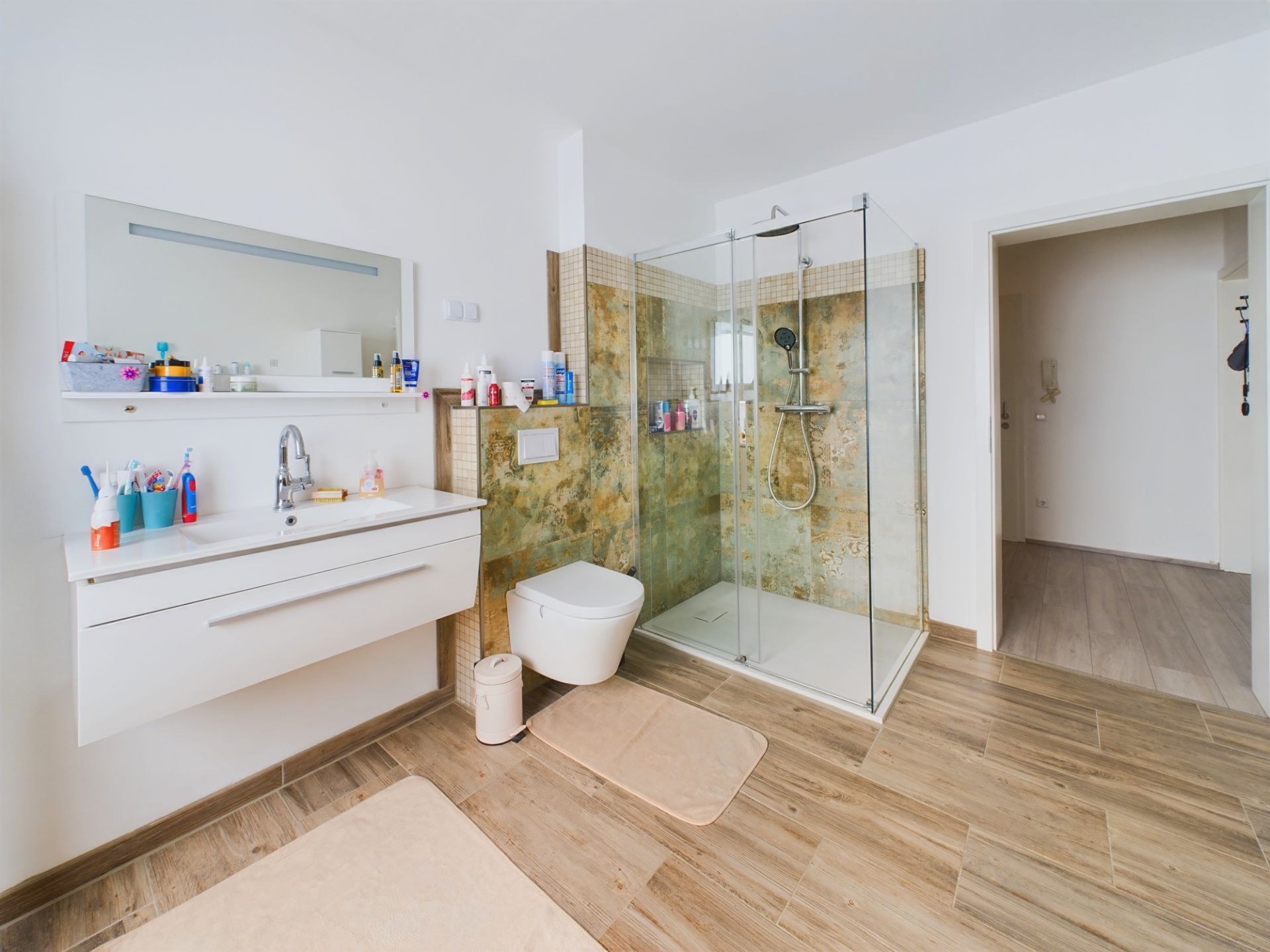 Modernes Bad mit Glasdusche, Waschbecken, großem Spiegel und WC auf Holzfußboden.