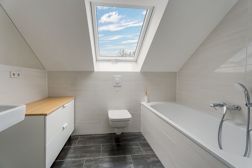Modernes Badezimmer mit Dachfenster, Badewanne, Hängetoilette und Waschbecken.