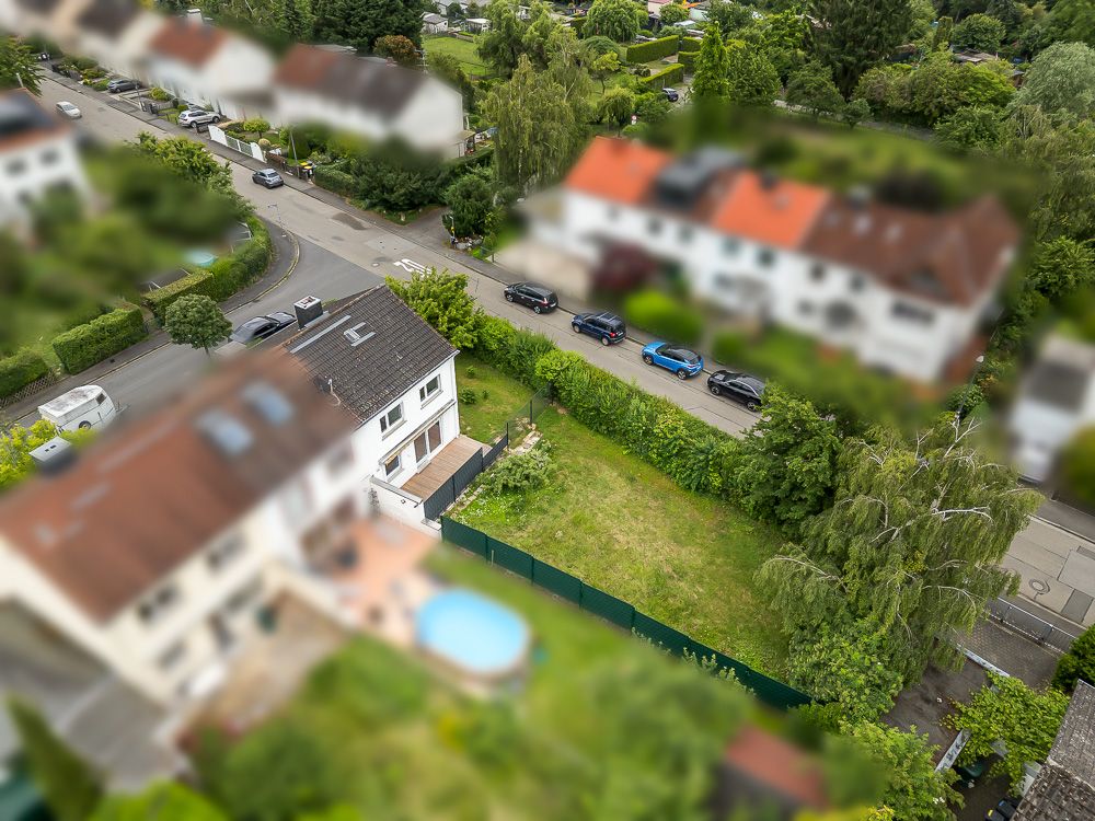 Luftaufnahme eines Wohnhauses mit Garten und angrenzender Straße mit parkenden Autos.
