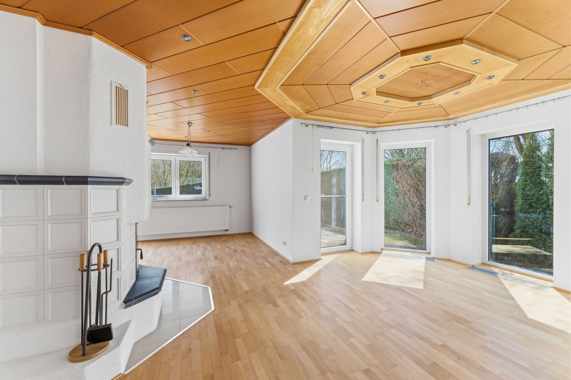 Helles Wohnzimmer mit Holzdecke, Kamin, großen Fenstern und Parkettboden.