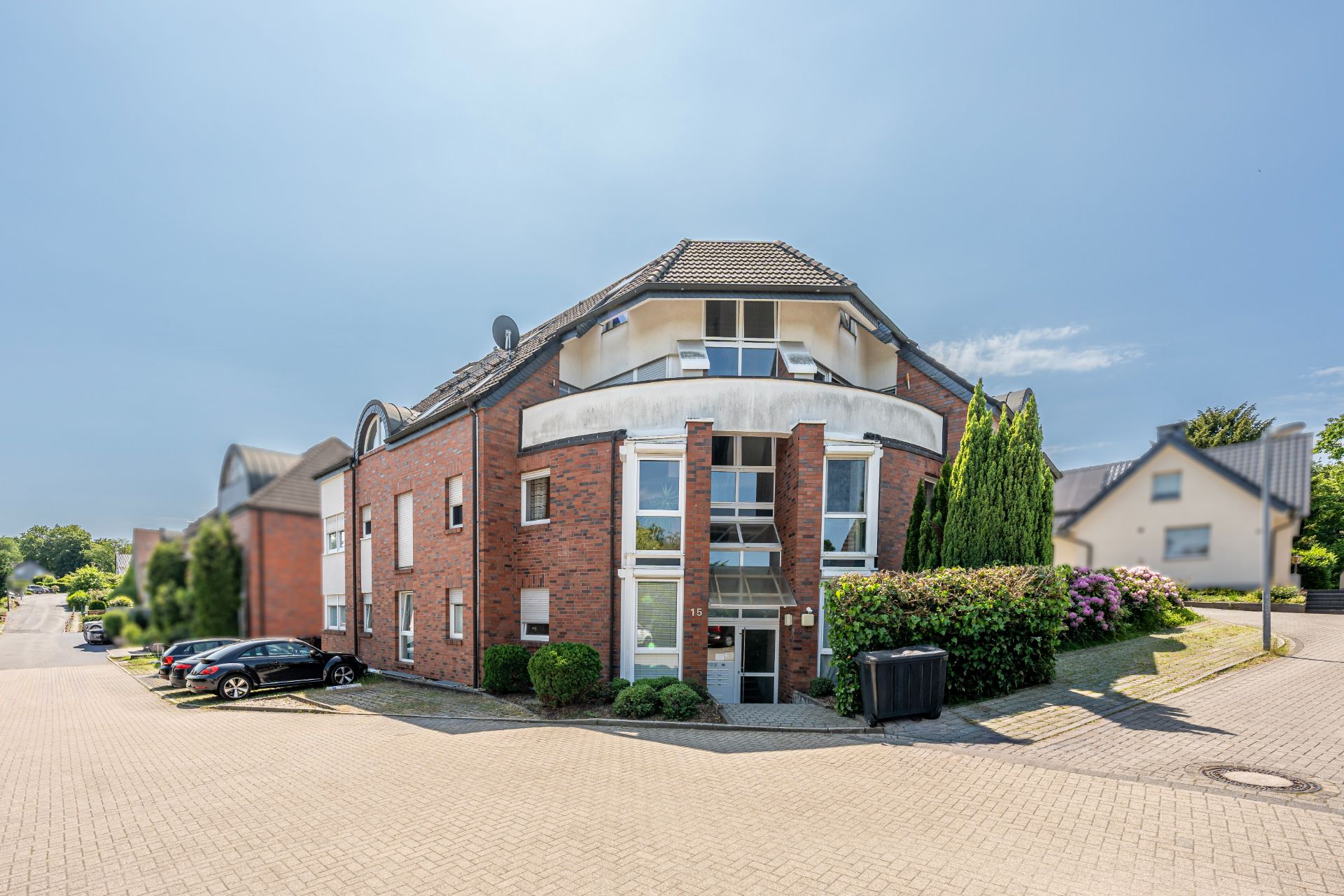 Modernes, rotes Mehrfamilienhaus mit großen Fenstern, Balkon und parkenden Autos davor.