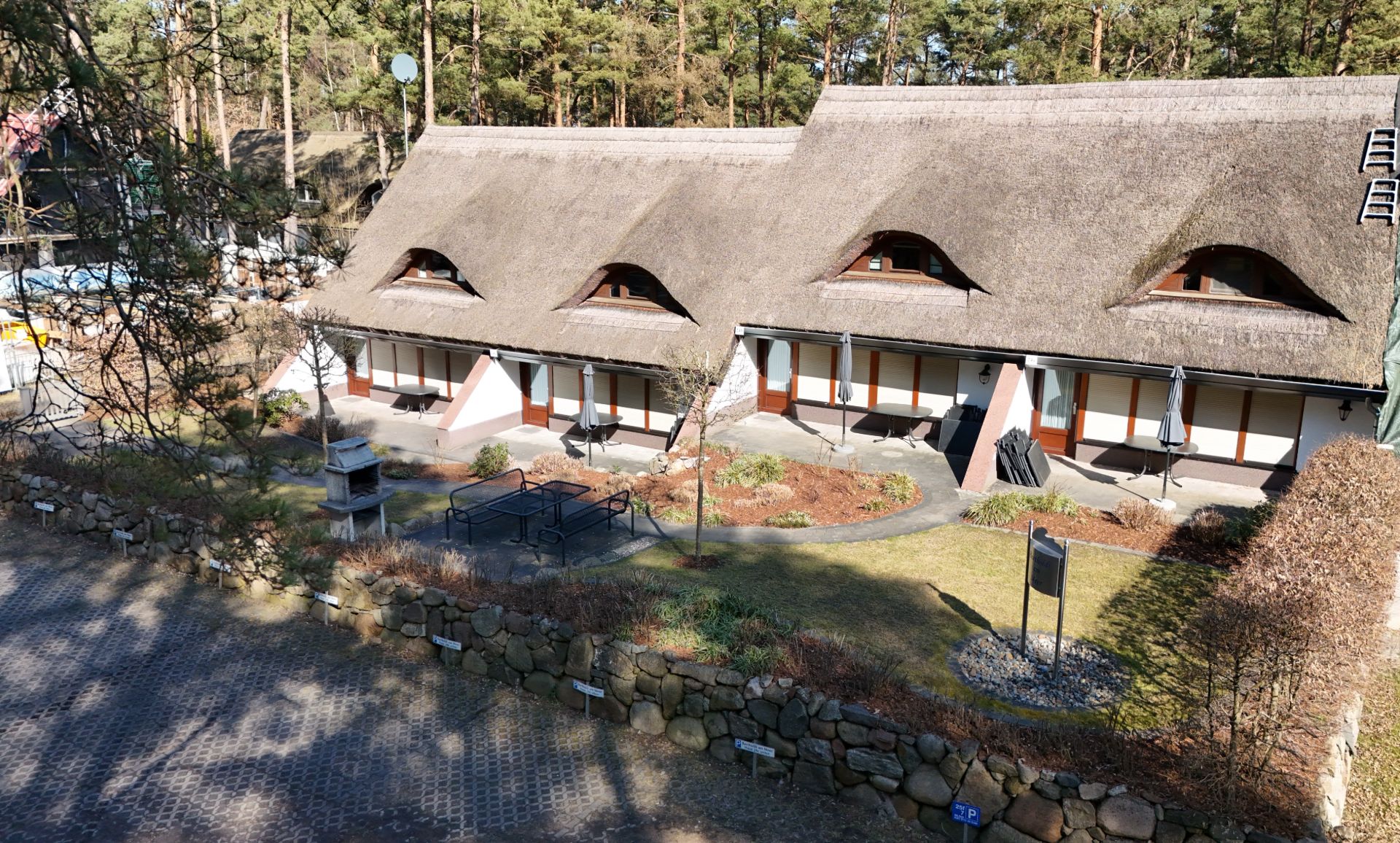Reetgedecktes Wohnhaus mit drei Eingängen und Terrasse, umgeben von Garten und Steinmauer.