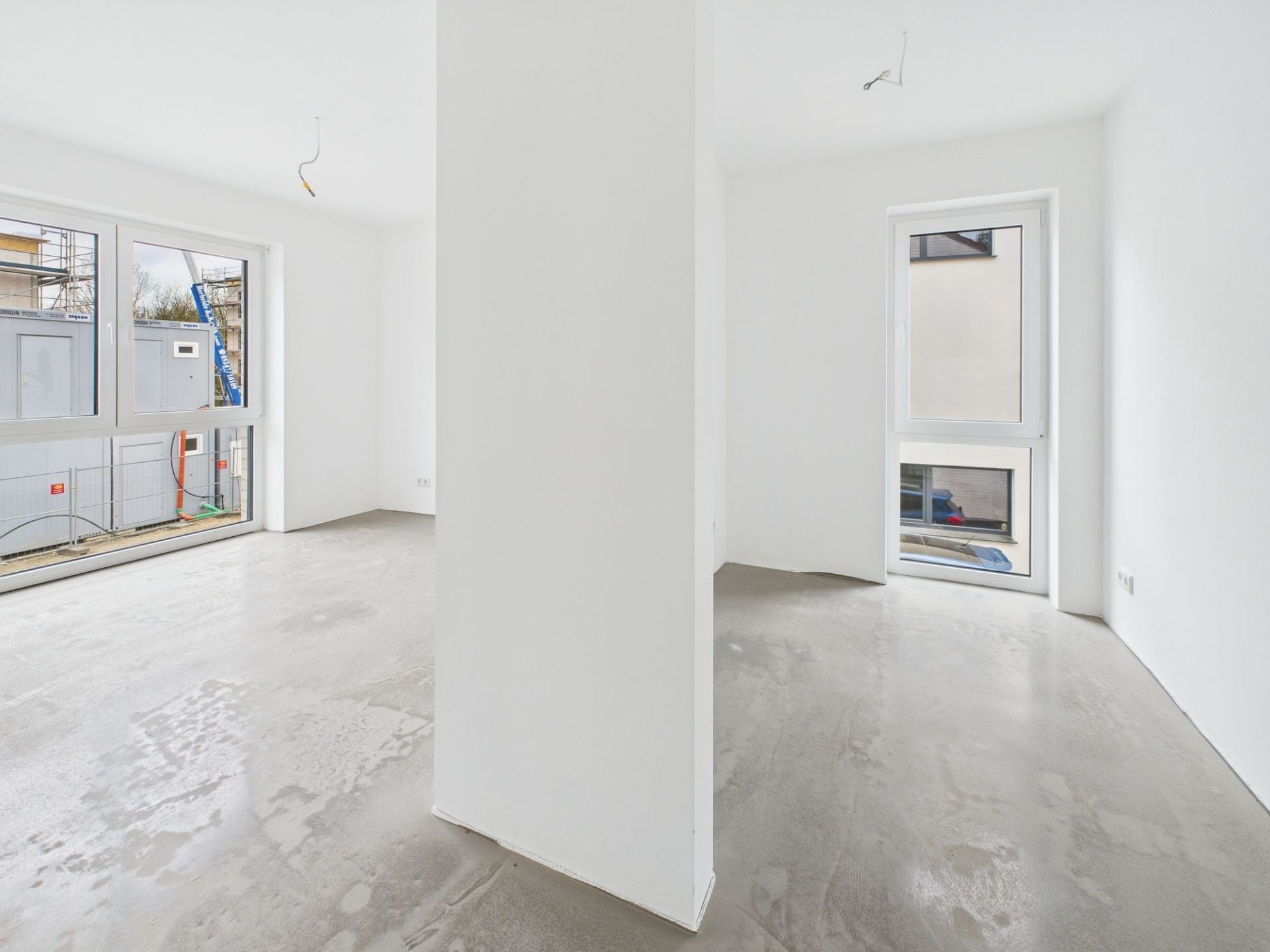 Heller, leerer Raum mit weißen Wänden, Betonboden und großen Fenstern.