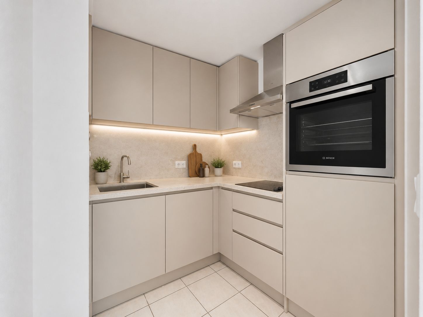 Moderne, beige Einbauküche mit Herd, Ofen, Spüle und Oberschränken.