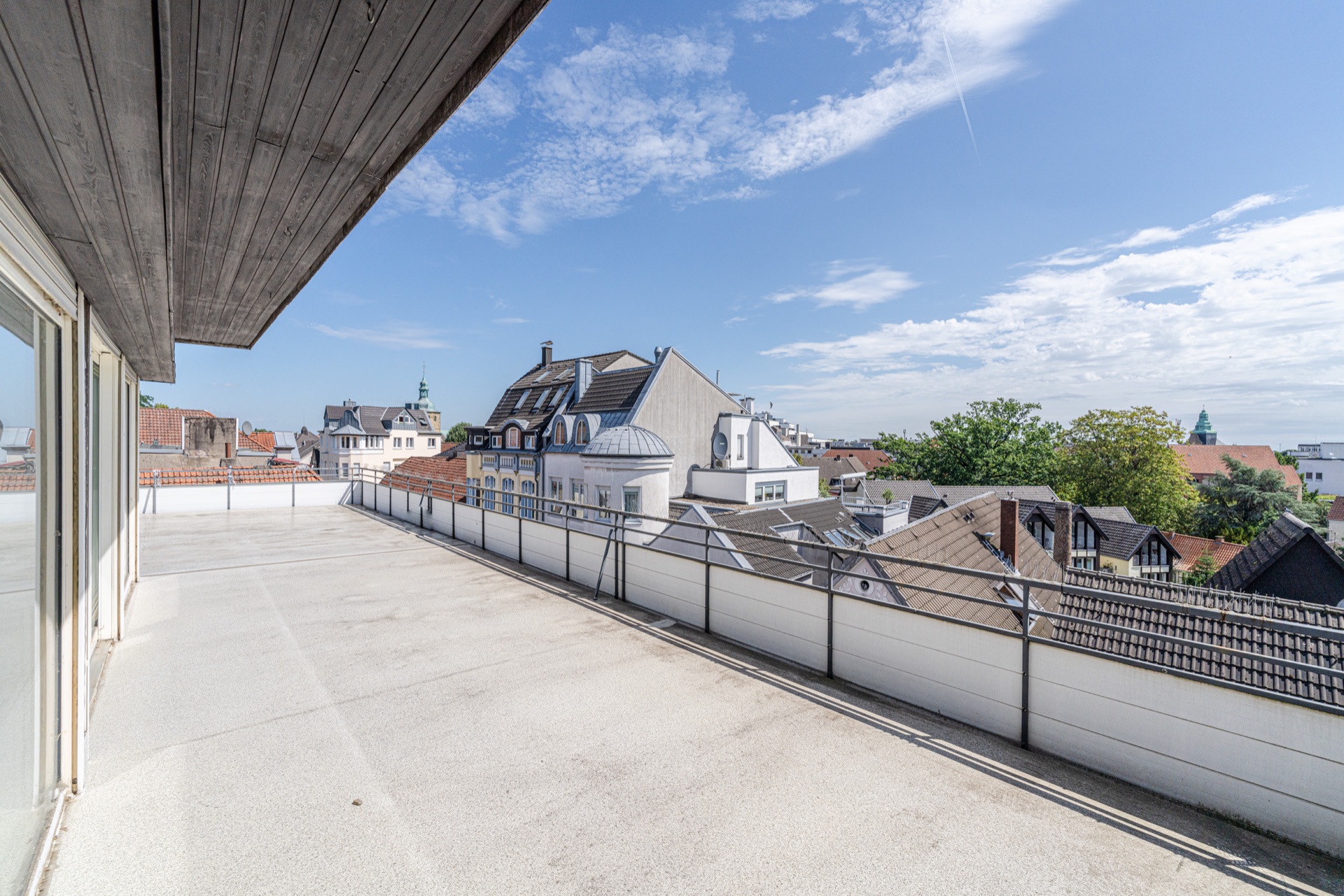Große Dachterrasse mit Geländer und Blick auf Nachbarhäuser unter blauem Himmel.