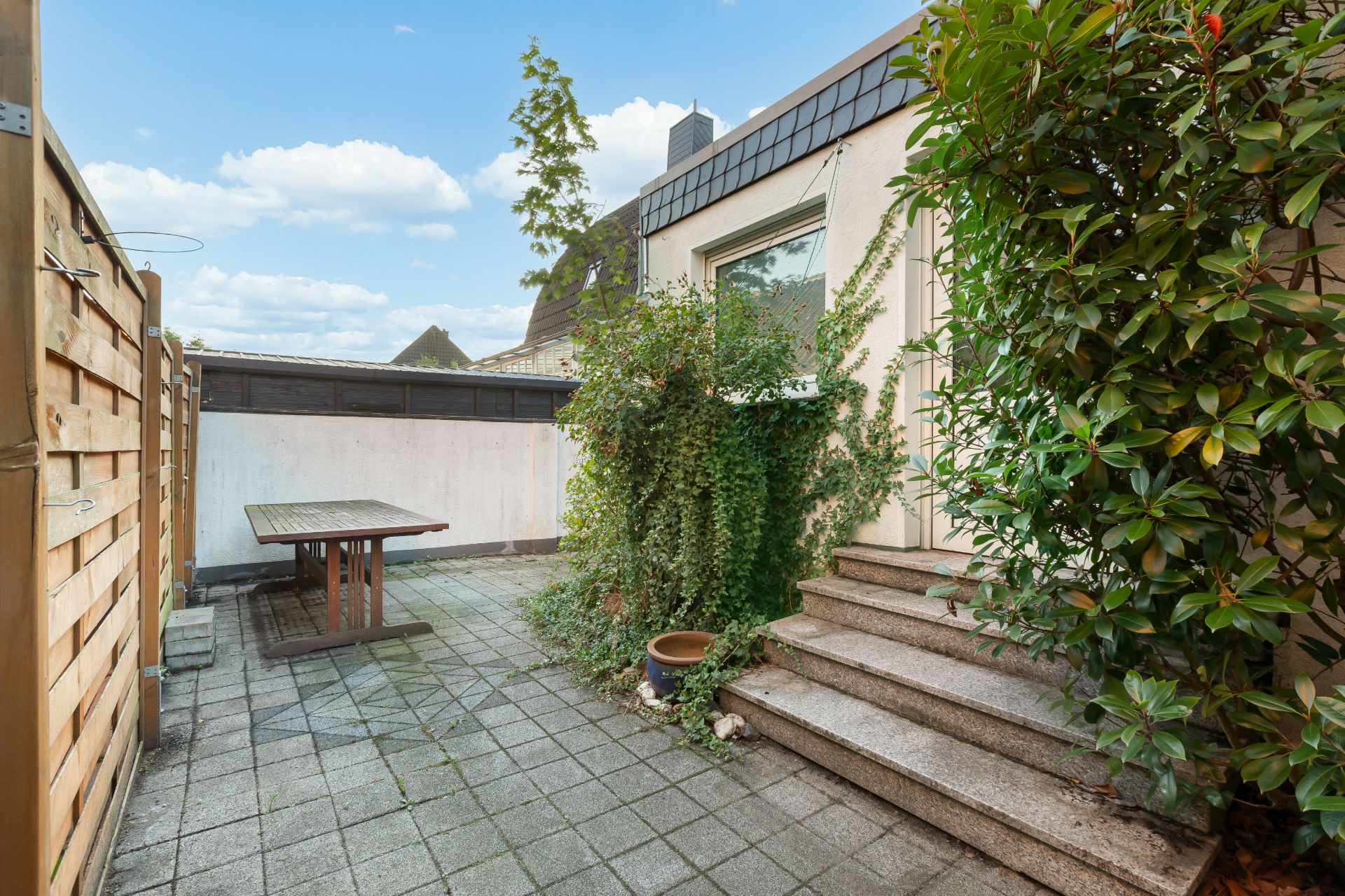 Kleiner Innenhof mit Steinplatten, Tisch, Pflanzen und Treppe zum Hauseingang.