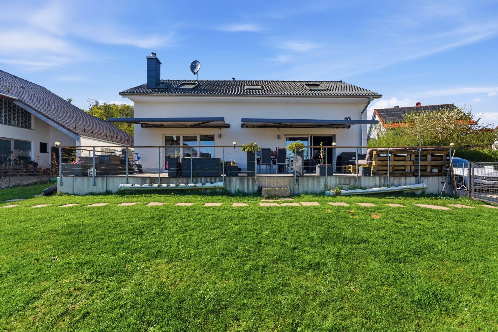 Moderne Doppelhaushälfte mit großer Terrasse und gepflegtem Garten bei sonnigem Wetter.