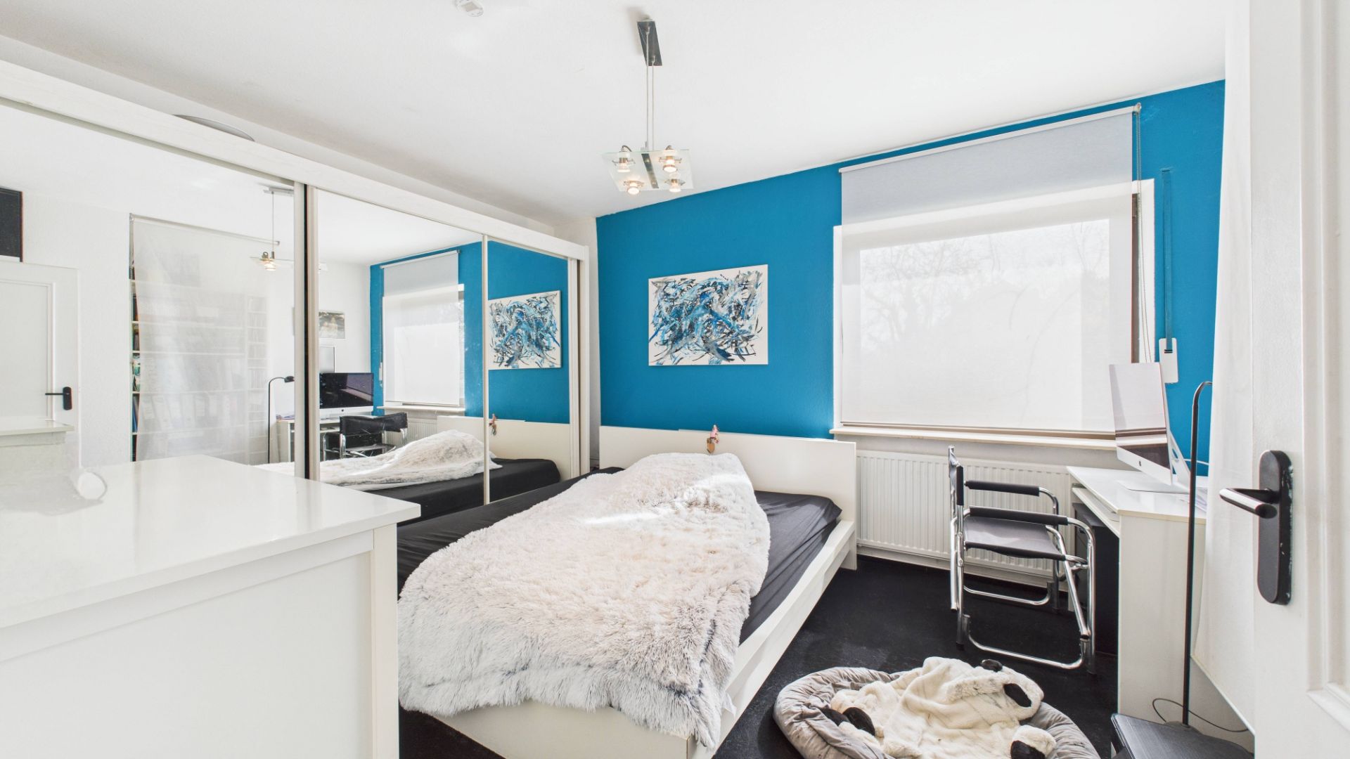Helles Schlafzimmer mit blau gestrichener Wand, Bett, Schreibtisch, Spiegel-Schrank und Hundebett.