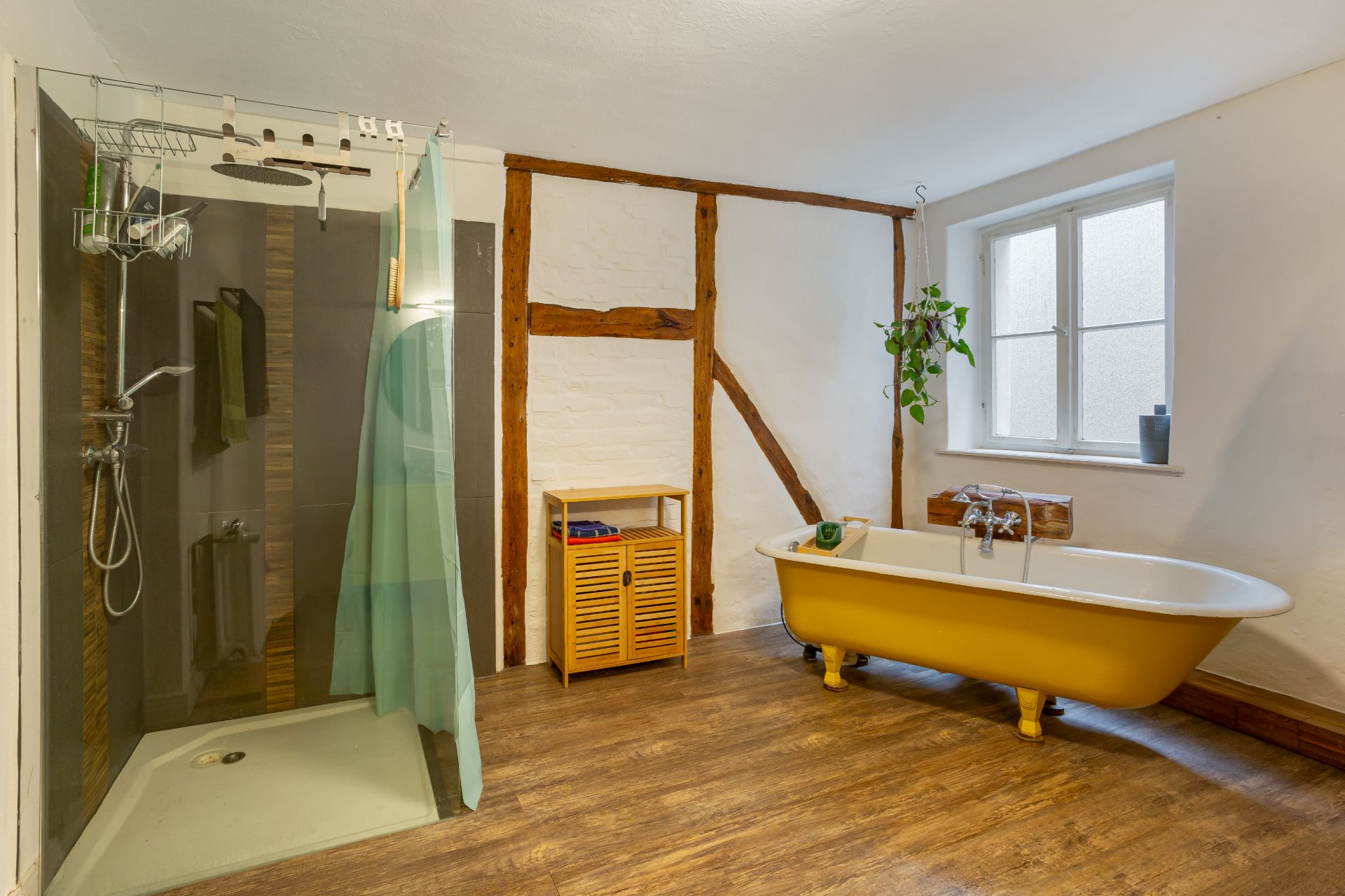 Badezimmer mit gelber Badewanne, Dusche, Fenster und Holzfußboden.