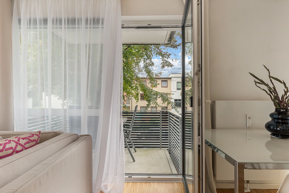 Wohnzimmer mit Sofa, Tisch, geöffneter Balkontür und Blick auf Balkon mit Stuhl.