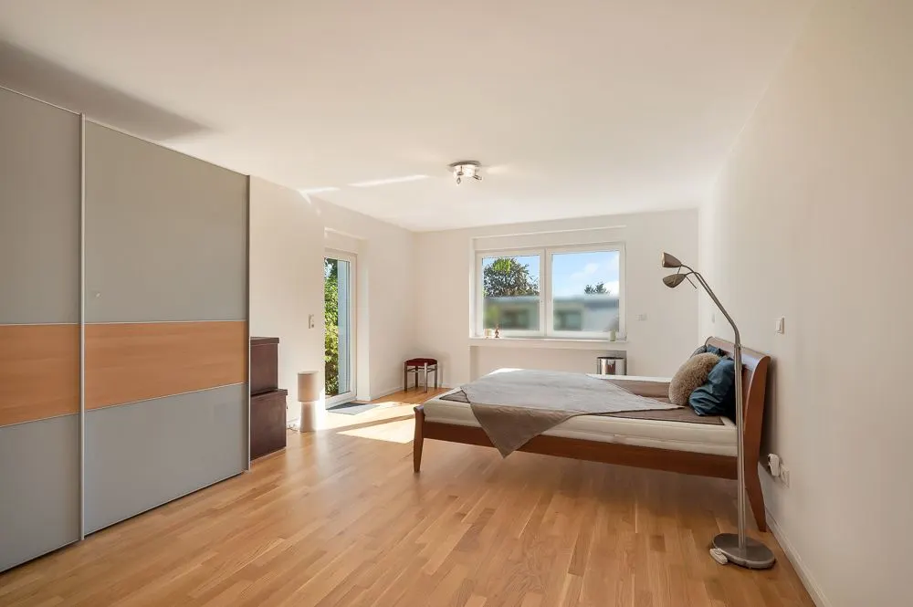 Helles Schlafzimmer mit Holzboden, Doppelbett, Kleiderschrank und großem Fenster.