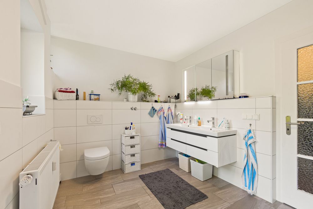 Modernes Badezimmer mit Doppelwaschbecken, Wandtoilette, Spiegel und Pflanzen.
