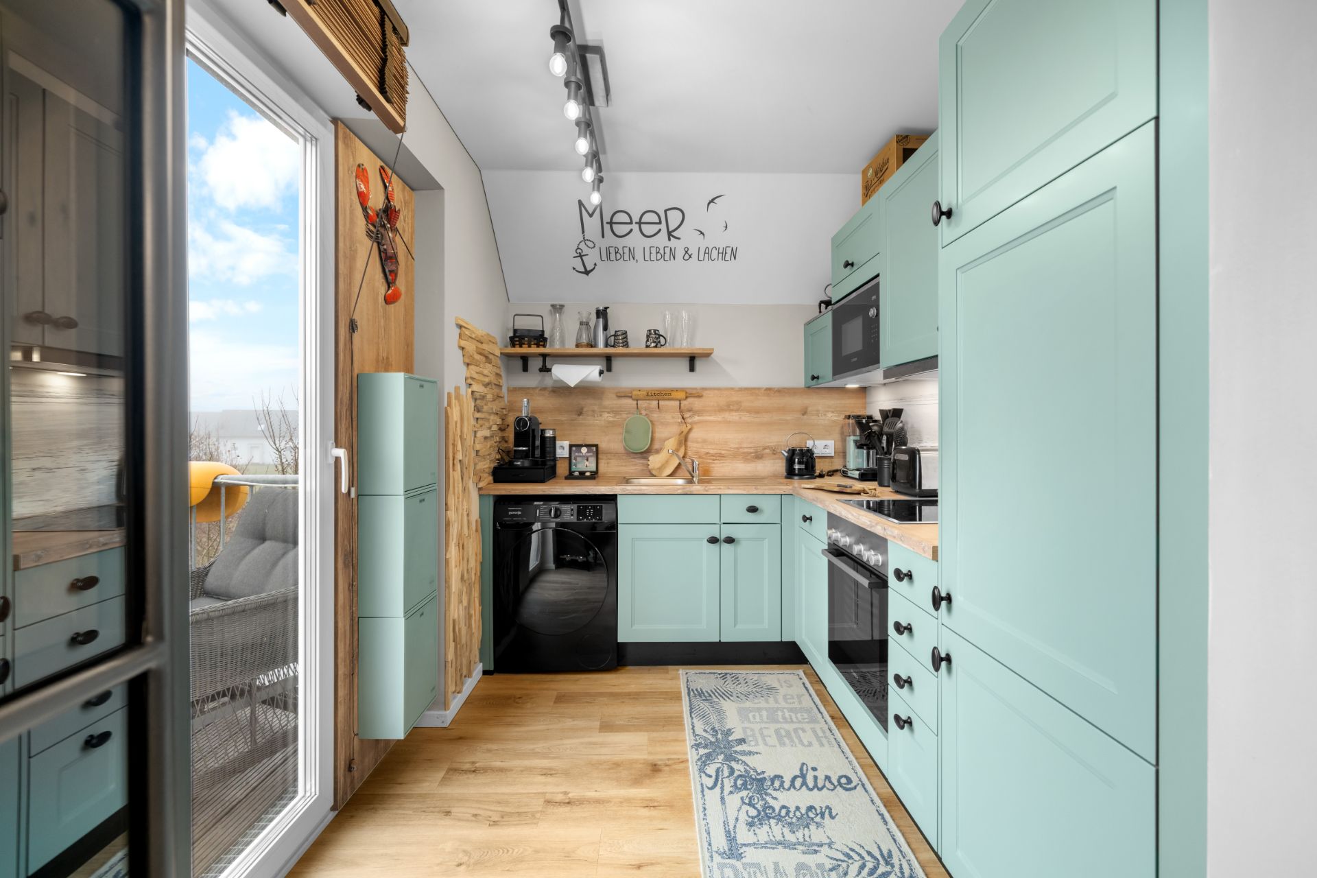 Moderne Küche mit mintfarbenen Schränken, Holzboden und großen Fenstern.