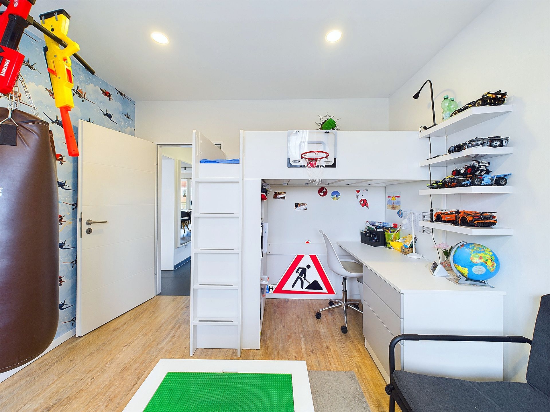 Kinderzimmer mit Hochbett, Schreibtisch, Hängeregalen, Boxsack und Spielzeugautos.