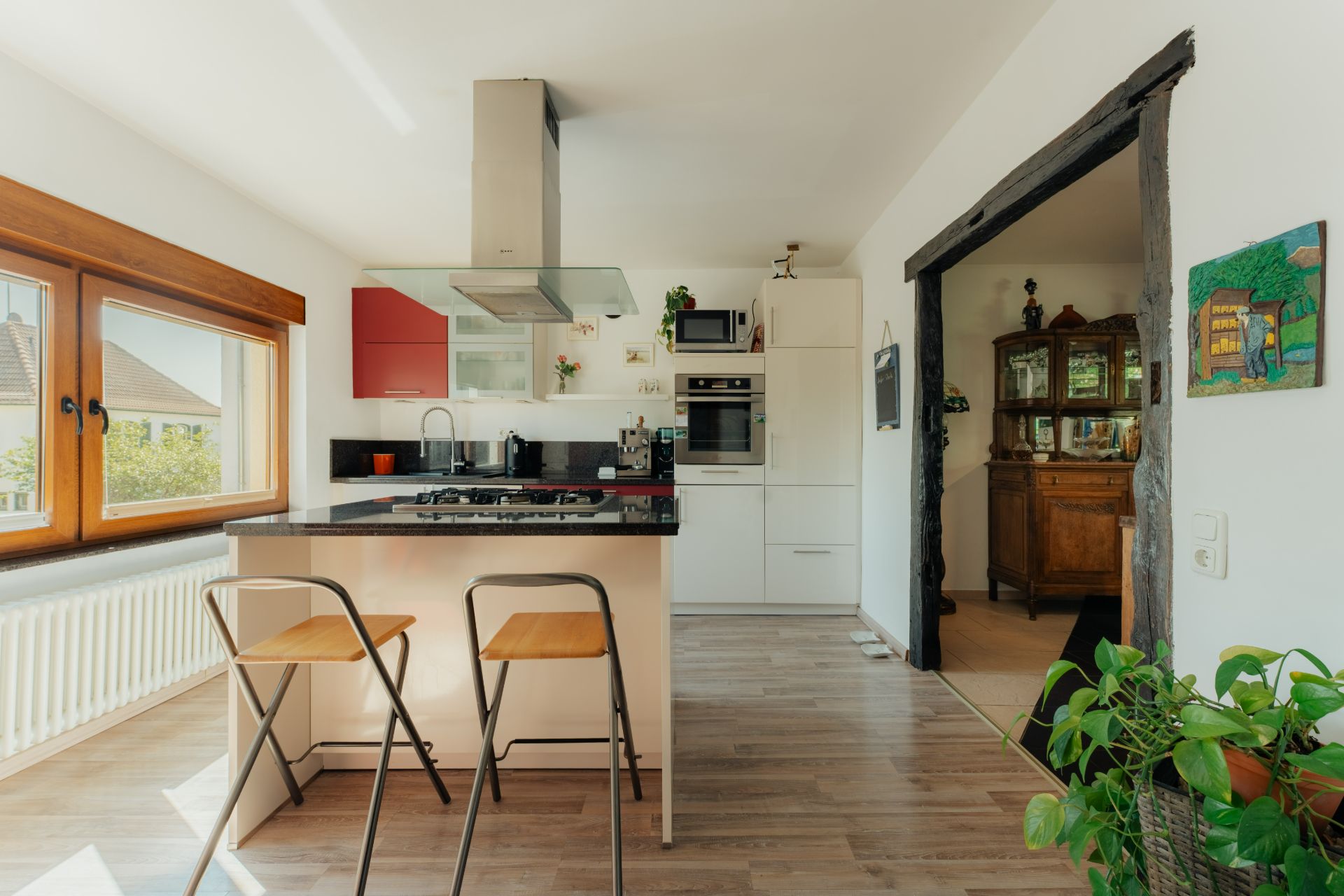 Moderne Küche mit Kücheninsel, zwei Hockern und großen Fenstern, angrenzend an ein Esszimmer.
