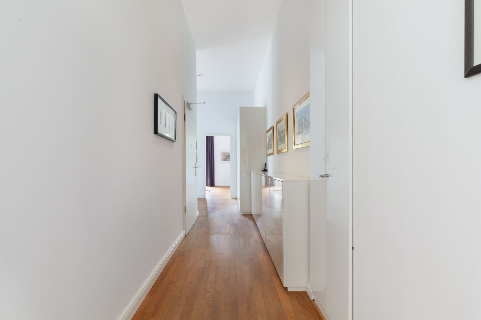 Heller Flur mit Holzfußboden, weißen Wänden und an der Wand hängenden Bildern.