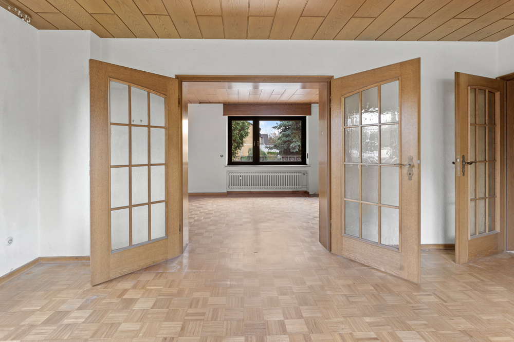 Heller Raum mit Holzboden, Holztüren und großem Fenster mit Blick nach draußen.