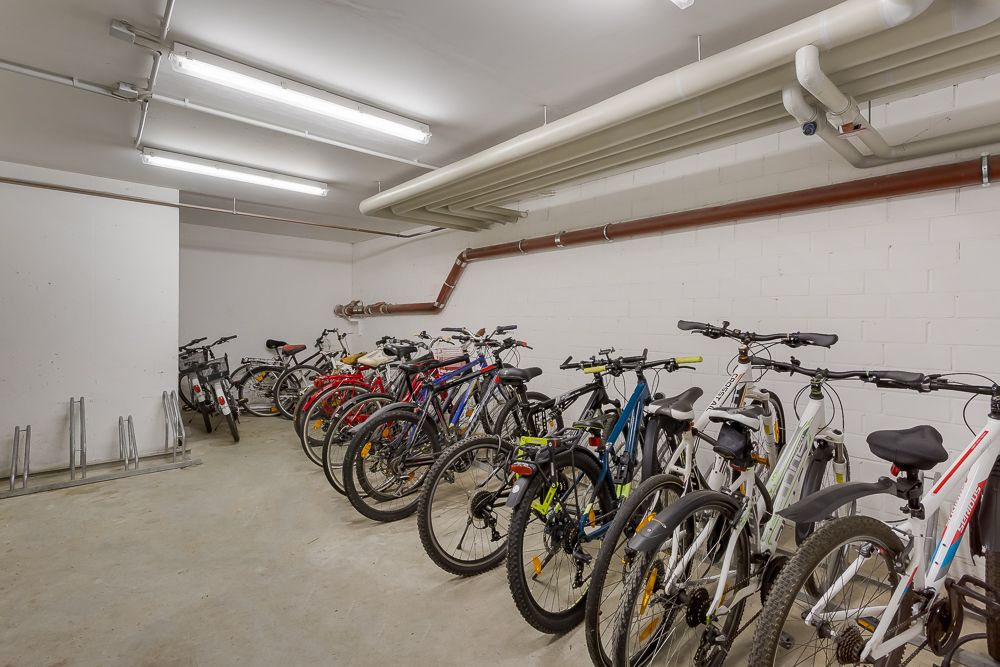 Fahrradraum mit mehreren geparkten Fahrrädern und Fahrradständern an den Wänden.
