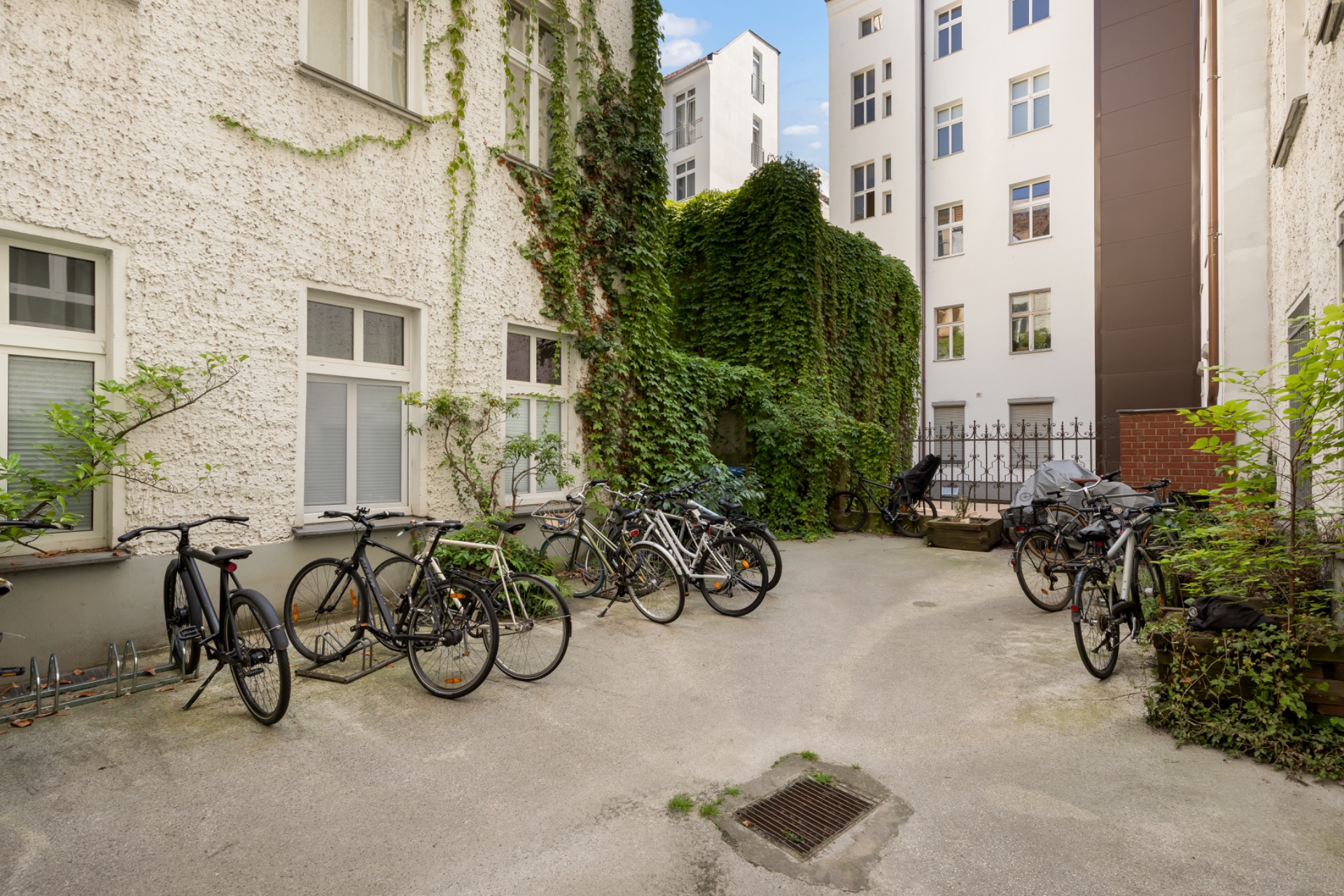 Innenhof mit Fahrrädern, umgeben von hellen Wohngebäuden, einige Wände mit Efeu bewachsen.