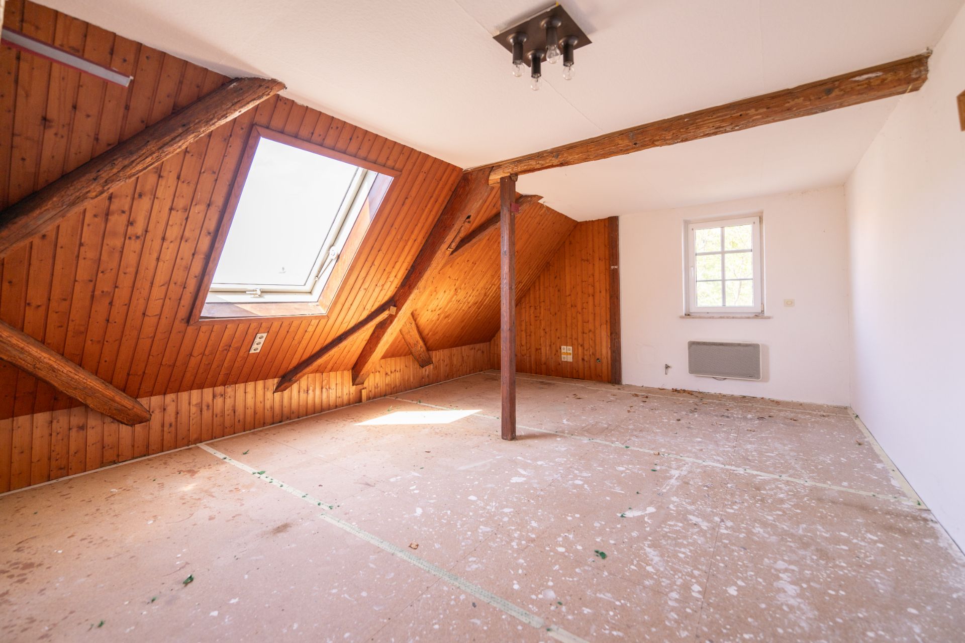 Leerer Dachbodenraum mit Holzbalken, Dachfenster und weißer Wand.