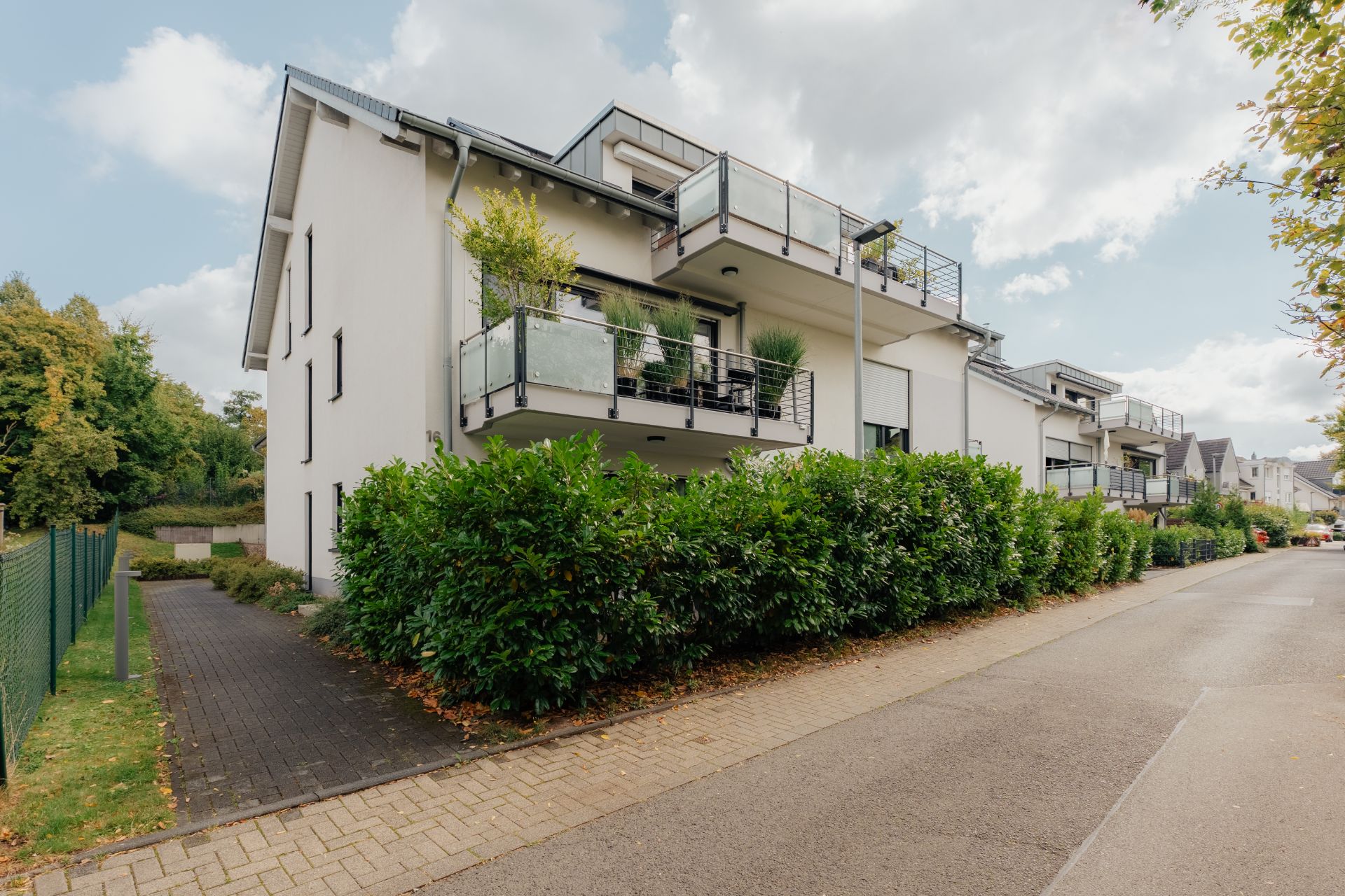 Modernes Wohngebäude mit Balkonen und grünen Büschen an einer ruhigen Straße.