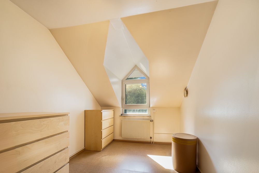 Kleines Zimmer mit Dachschräge, zwei Kommoden, Fenster und Mülleimer.