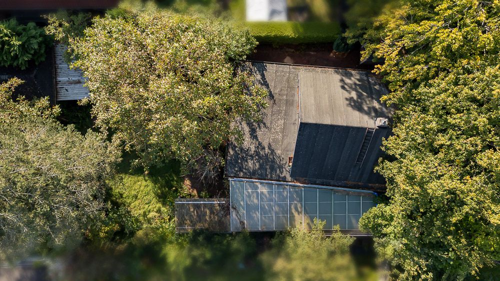 Luftaufnahme eines Hauses mit grauem Dach, umgeben von Bäumen und viel Grün.