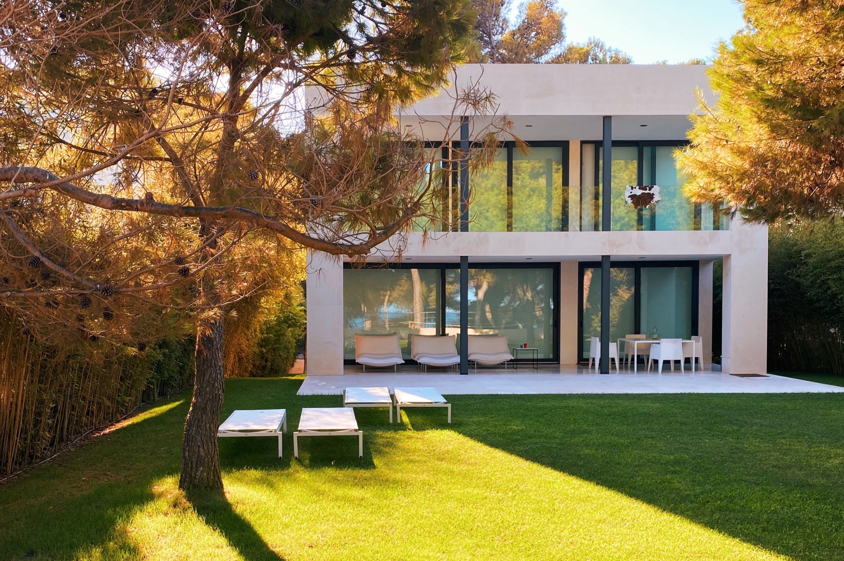 Modernes zweistöckiges Haus mit großer Terrasse und Garten, umgeben von Bäumen.
