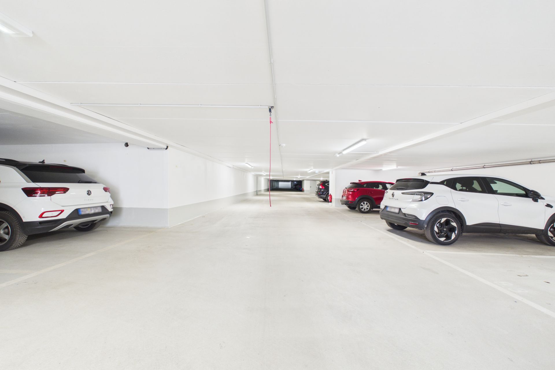 Helle Tiefgarage mit mehreren geparkten Autos und weiß gestrichenen Wänden.