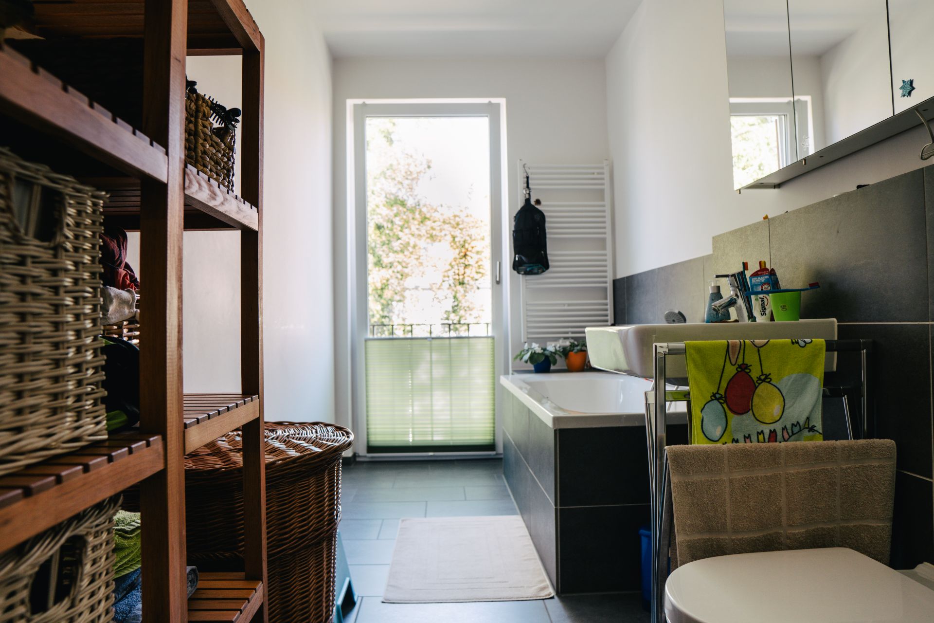 Modernes Badezimmer mit Badewanne, Regal mit Körben, Fenster und Handtuchhalter.