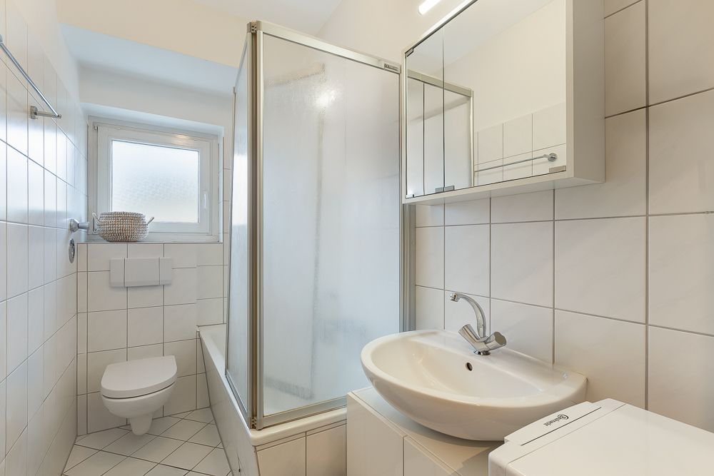 Helles Badezimmer mit Dusche, WC, Waschbecken und Spiegelschrank, alles gefliest.