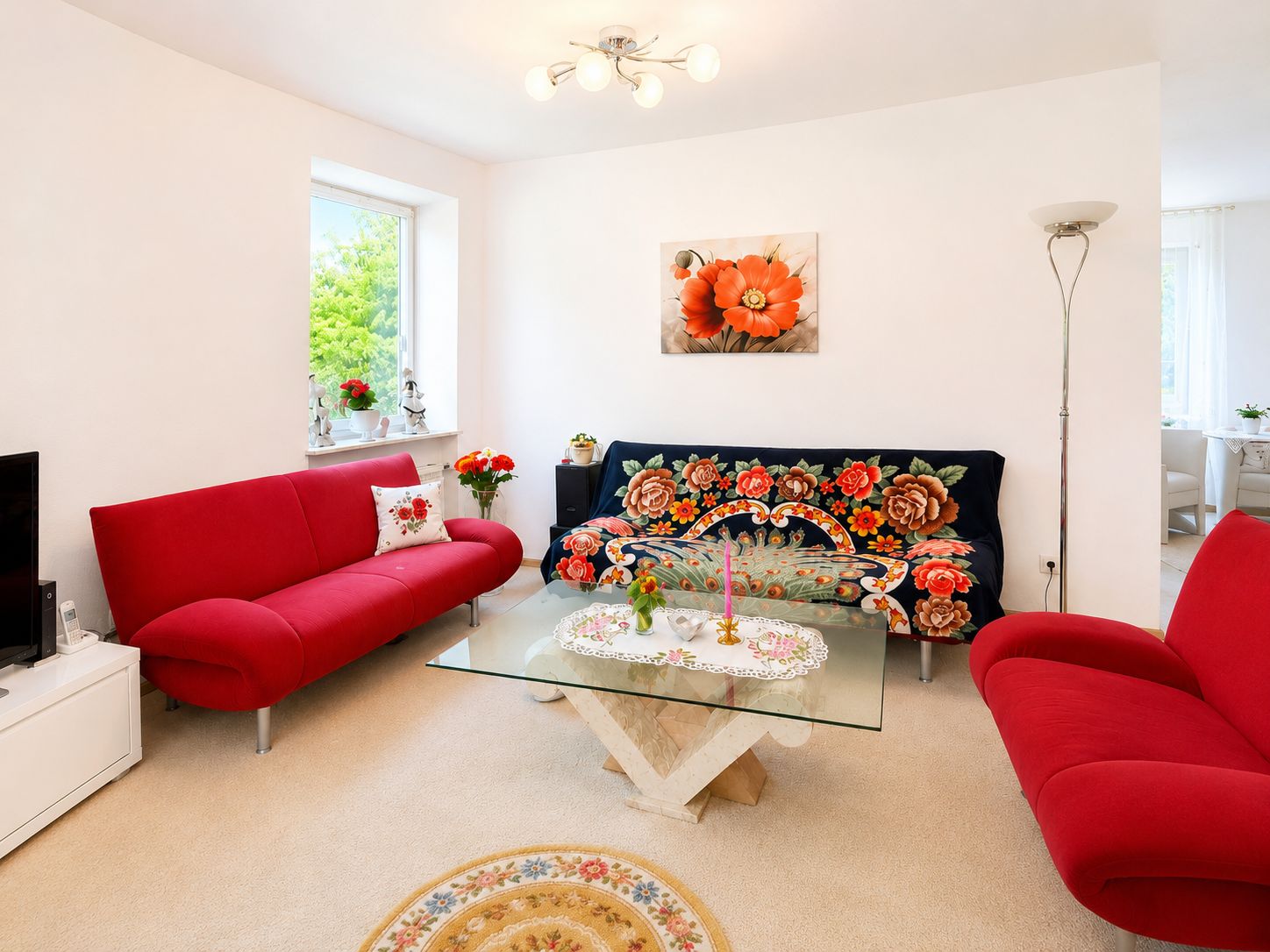 Helles Wohnzimmer mit roten Sofas, Glastisch und floralem Bild an der Wand.
