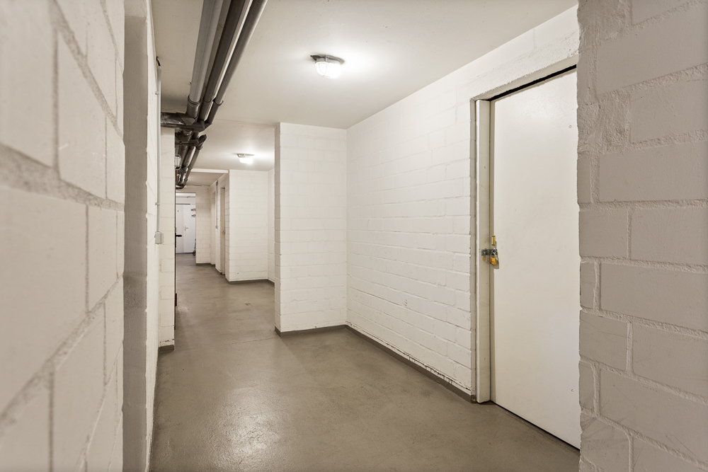 Heller Flur mit weißen Wänden, mehreren Türen und sichtbaren Rohrleitungen an der Decke.