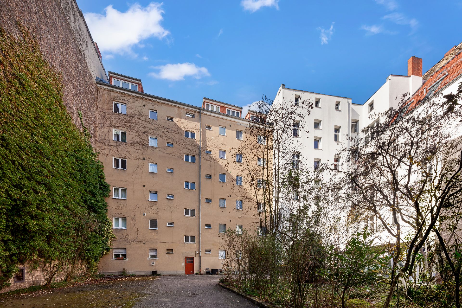 Mehrstöckiges Wohnhaus mit Innenhof und Bäumen, umgeben von anderen Gebäuden.