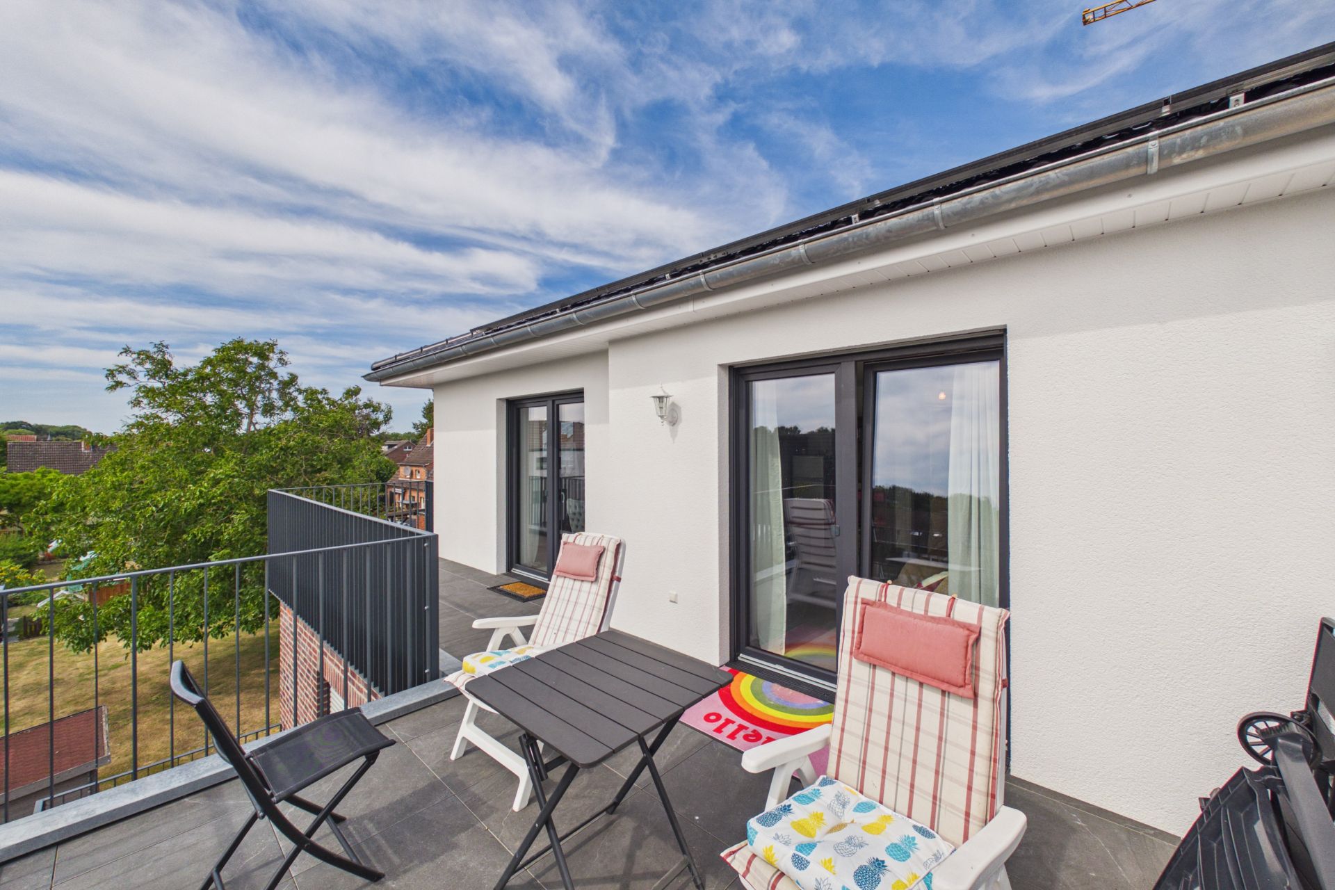 Möblierter Balkon mit Tisch, Stühlen und zwei Liegestühlen an einem modernen Wohnhaus.