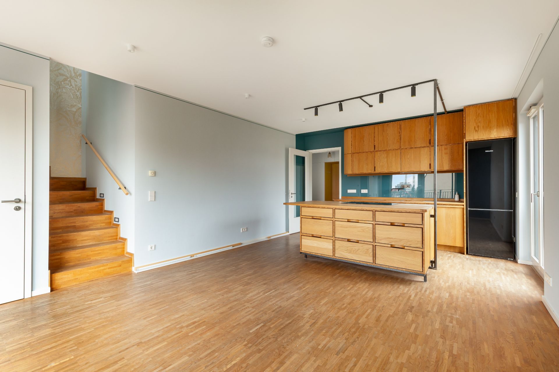 Leere Wohnküche mit Holzboden, moderner Einbauküche und Treppe im Hintergrund.