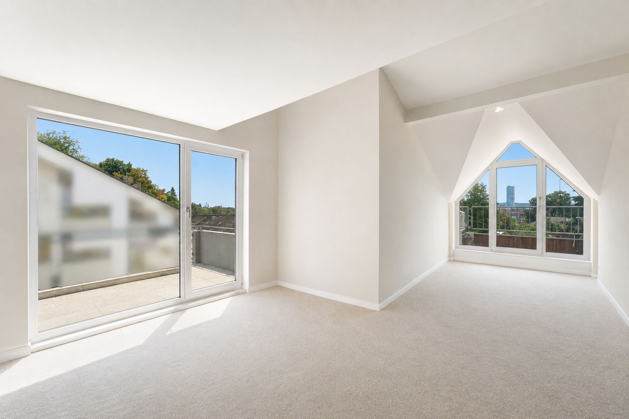 Helles Zimmer mit Teppichboden, großen Fenstern und Zugang zu einem Balkon.