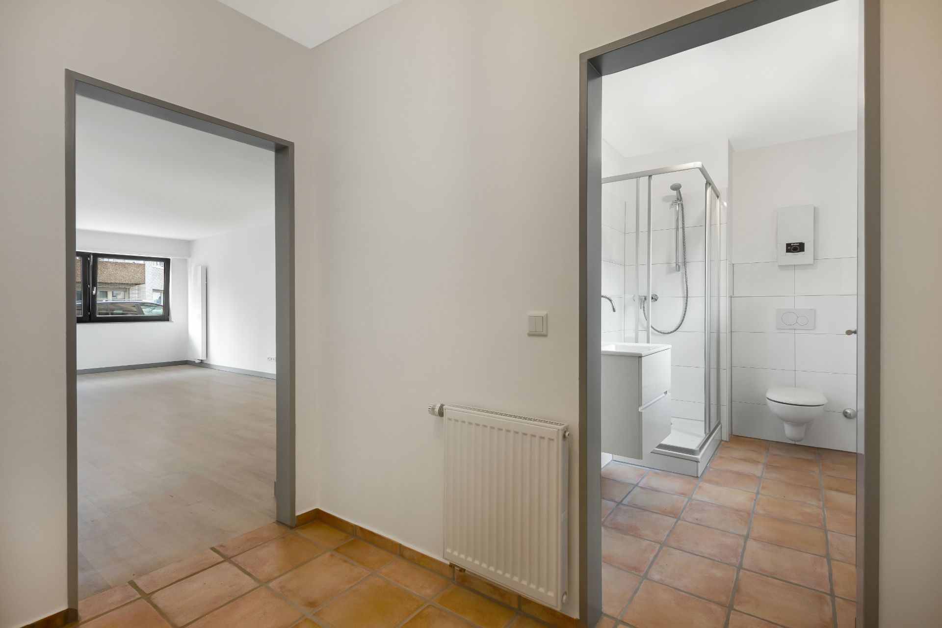 Flur mit Blick in ein Wohnzimmer und ein Badezimmer mit Dusche und Toilette.