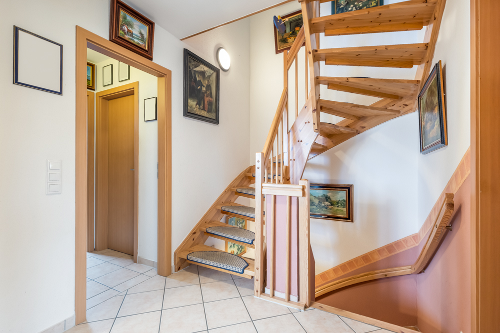 Holztreppe in einem Flur mit Bildern an den Wänden und einer Tür links.