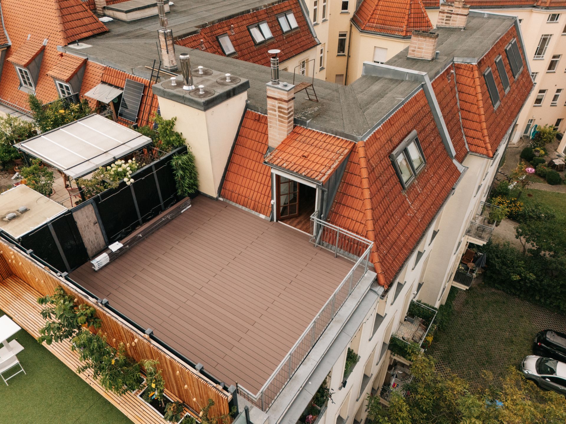 Dachterrasse mit Geländer und Zugangstür auf einem Wohngebäude mit roten Dachziegeln.