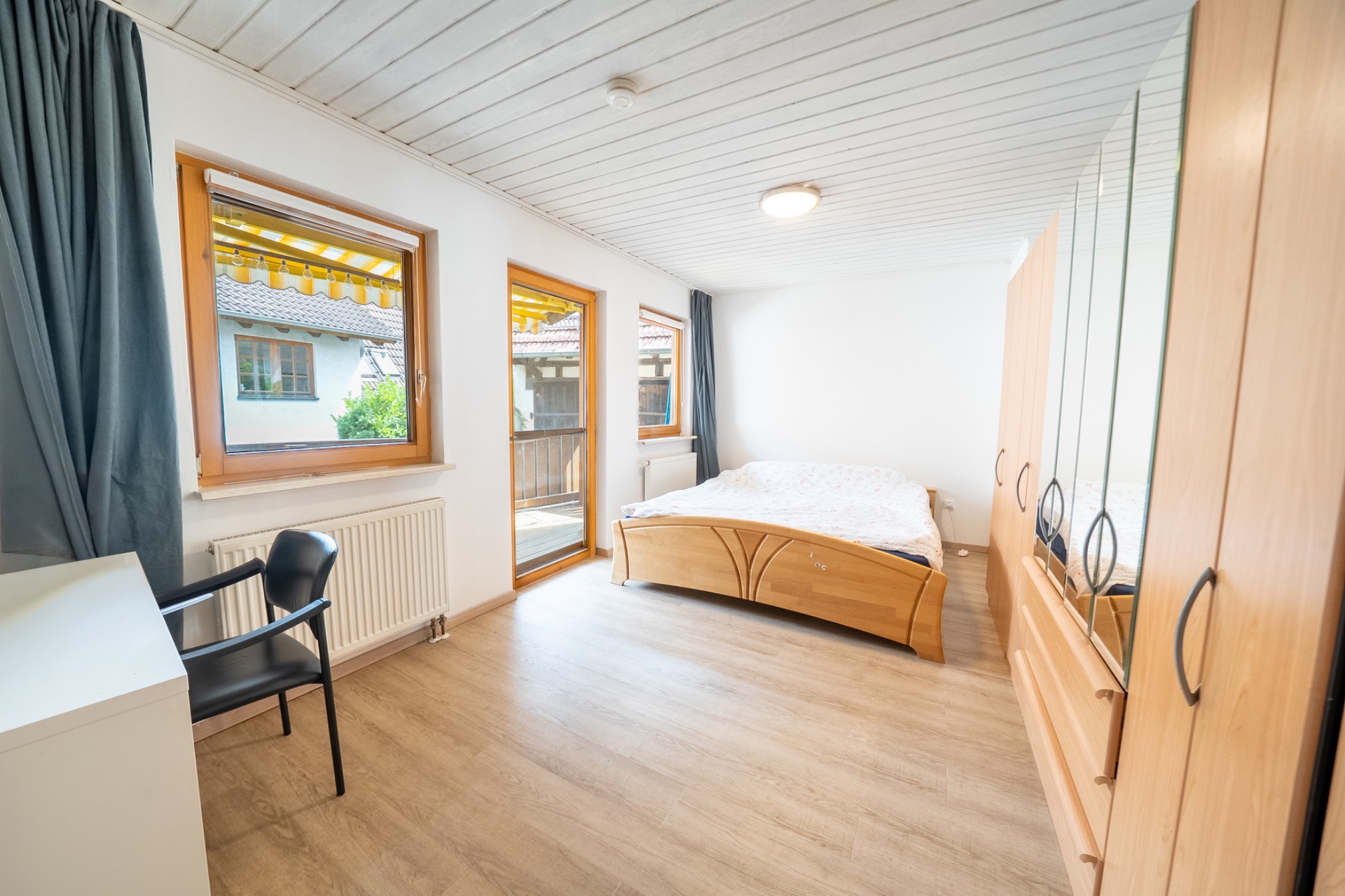 Helles Schlafzimmer mit Doppelbett, Kleiderschrank, Schreibtisch und Fensterfront.