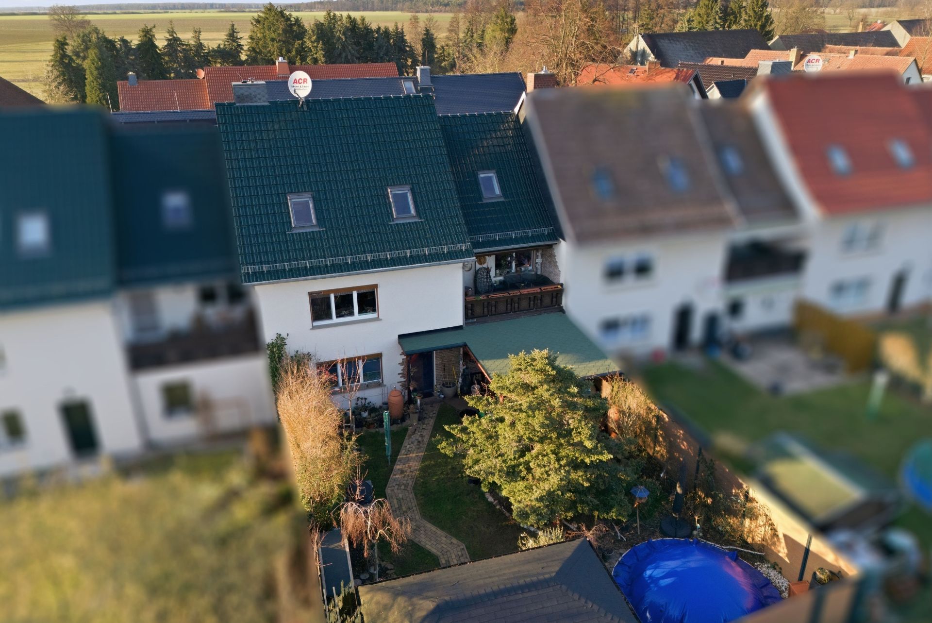 Reihenhaus mit grünem Dach und kleinem Garten mit Baum und Gartenweg.