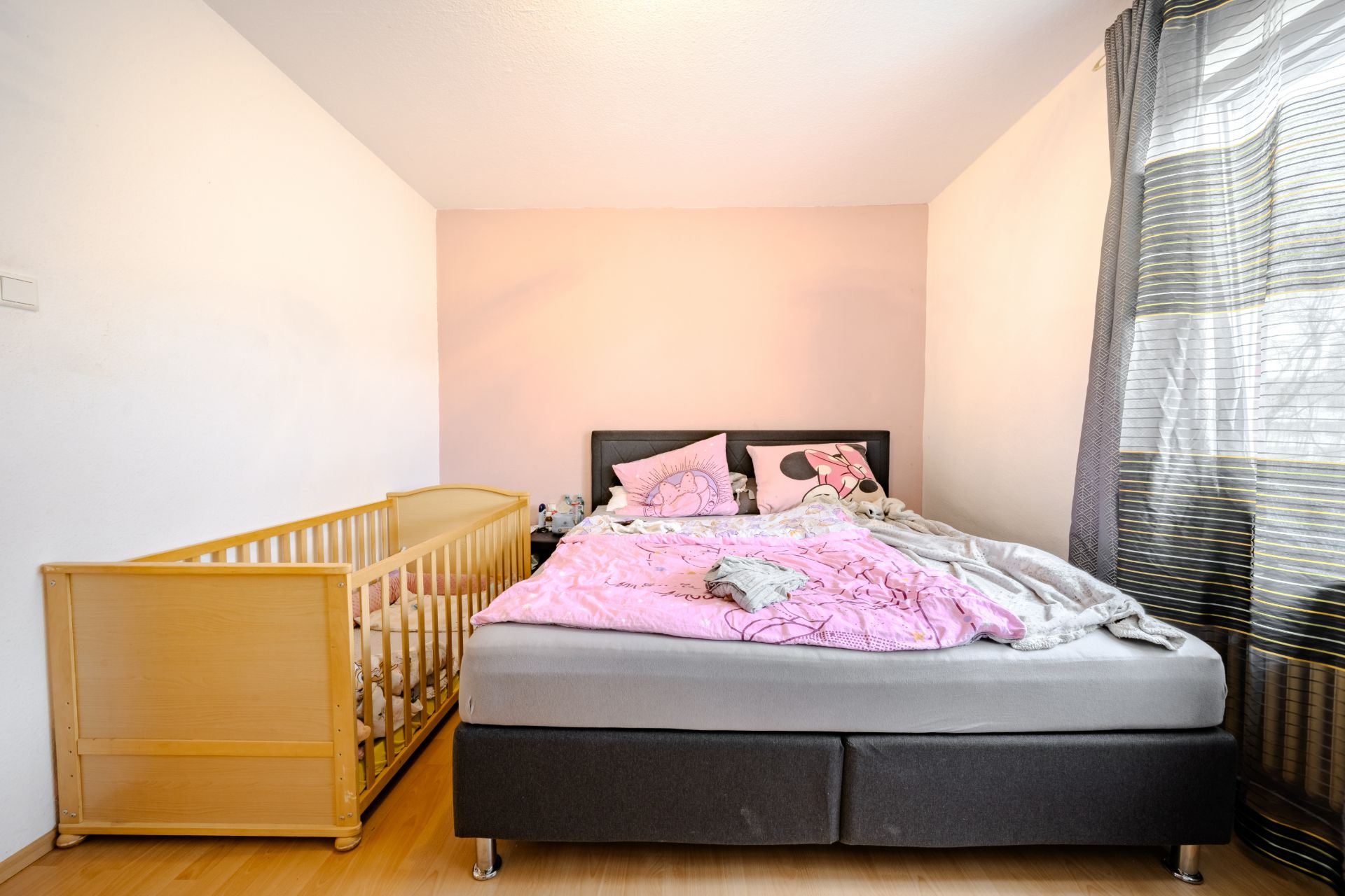 Schlafzimmer mit Doppelbett, rosa Bettwäsche und einem Babybett neben dem Bett.