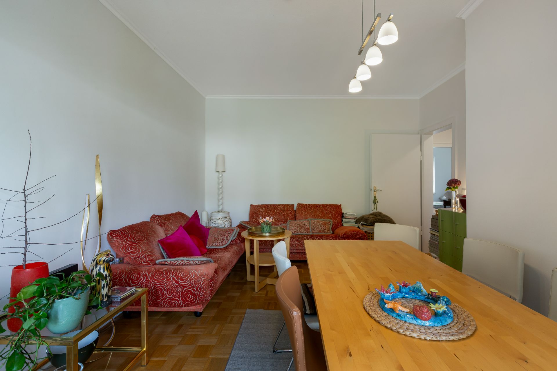 Wohnzimmer mit roten Sofas, Holztisch, Pflanzen und Deckenlampe.