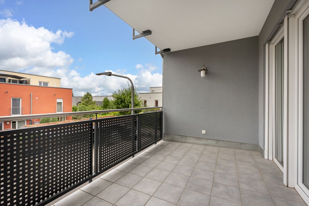 Geräumiger Balkon mit Fliesenboden und modernem Geländer, Blick auf Nachbargebäude und Himmel.