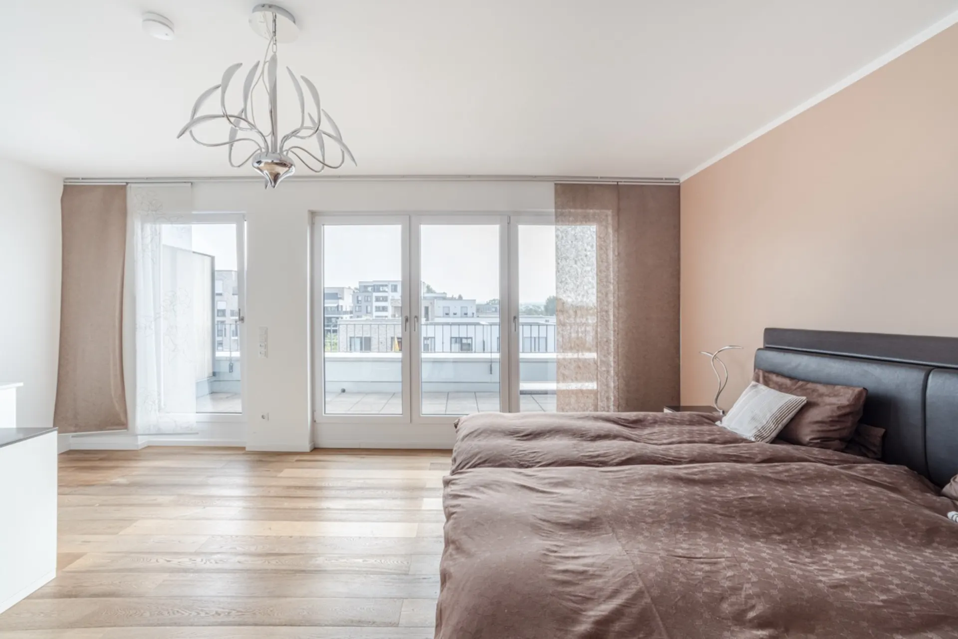 Helles Schlafzimmer mit großem Bett, Parkettboden und Zugang zu einem Balkon.